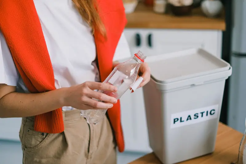 Woman placing plastic bottle into recycling bin in kitchen setting