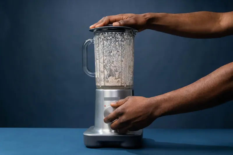 Close-up of male hands operating a blender in a kitchen setting
