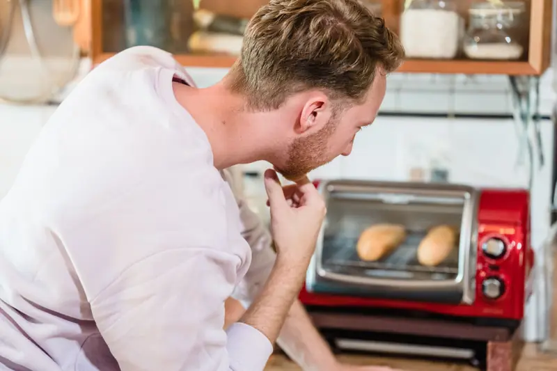 A man observes bread baking in a toaster oven in a cozy kitchen setting