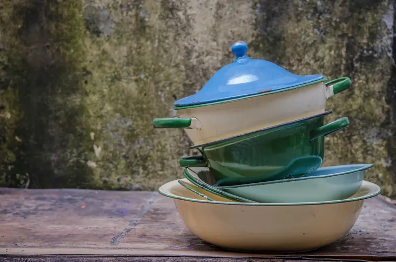A rustic stack of colorful vintage enamel pots and pans outdoors against a textured wall